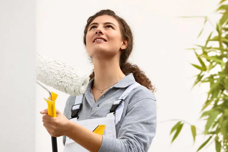 Stručna izvođačica, soboslikarica liči fasadu kuće valjkom, fasadna boja društva Sto